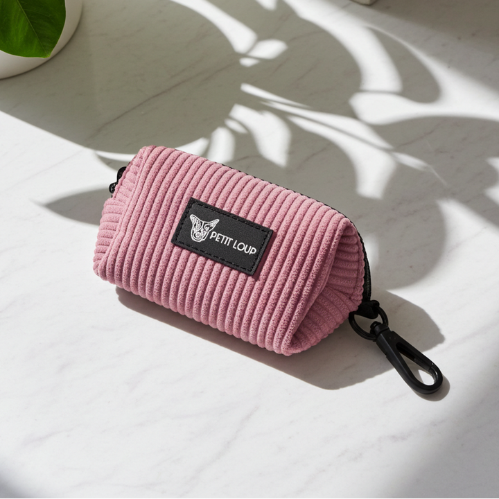 Pink corduroy pouch with a brand logo on a light wooden surface with a plant in the background.